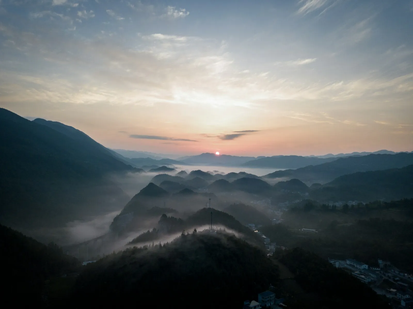 A soft sunrise glowing over layers of misty mountains