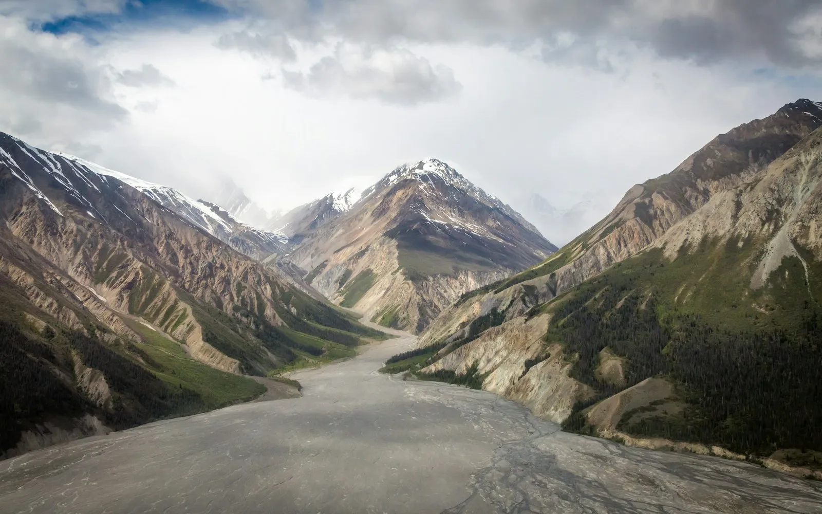 A broad glacial valley beneath snow-streaked mountains